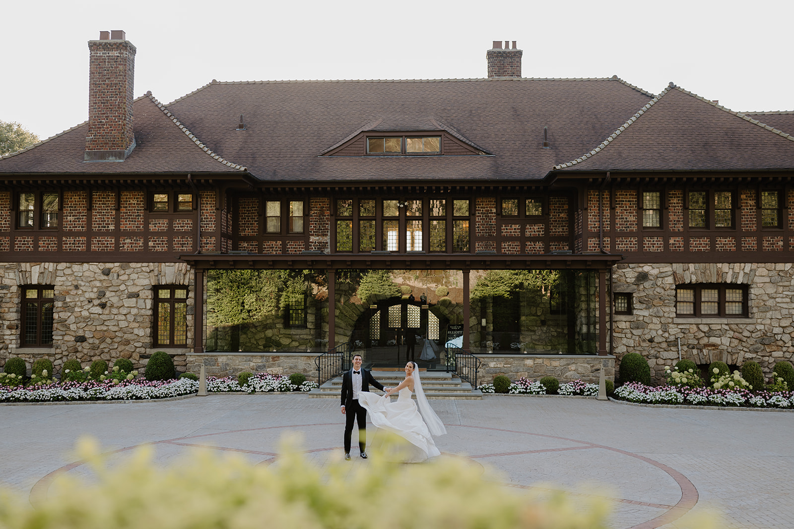 Newlyweds holding hands as the bride twirls in the brick courtyard in front of the Le Chateau mansion.
